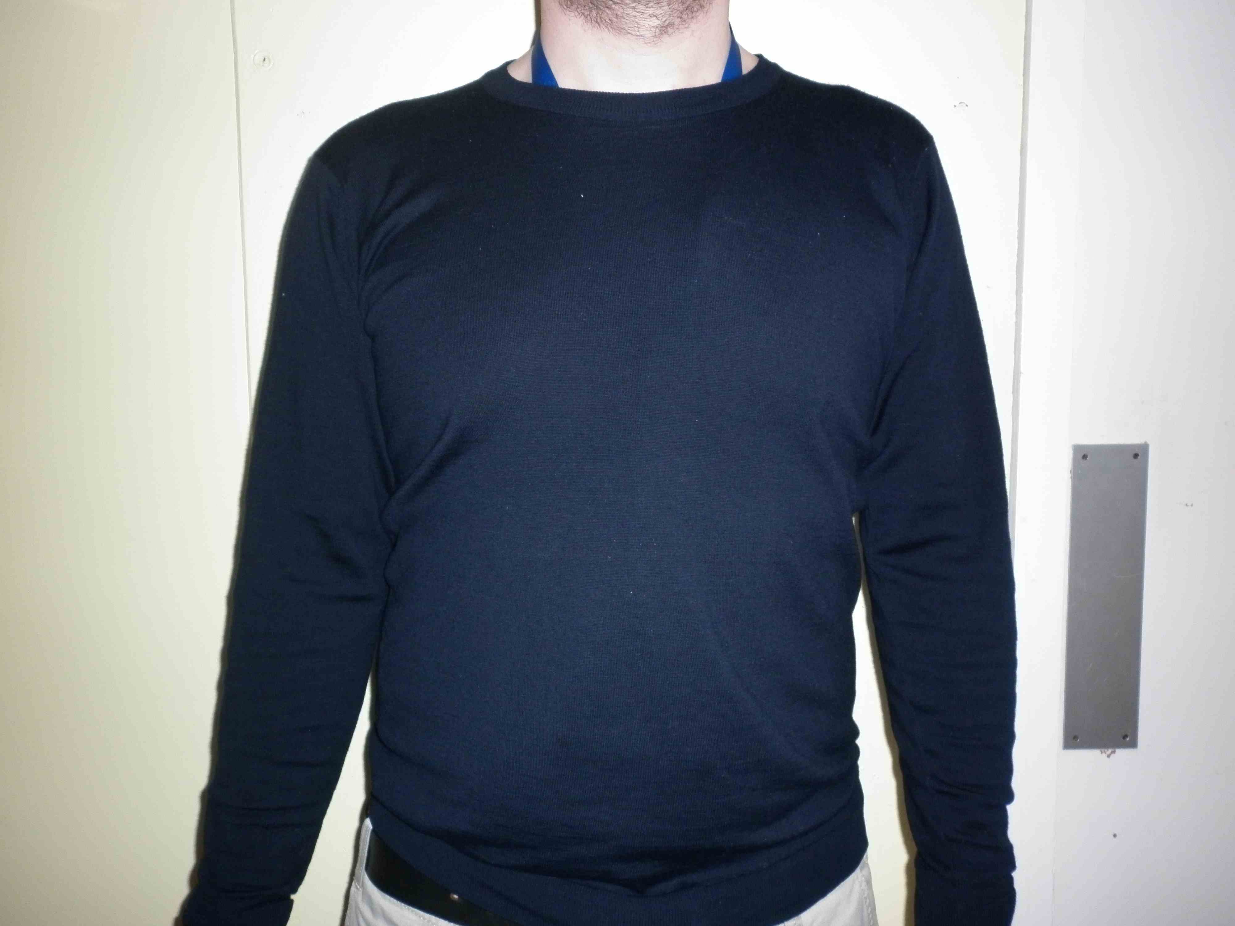 A man's trunk. He is wearing a plain, dark jumper, which provides good visual contrast with his hands. His ID badge is tucked into his jumper. He is standing in front of a plain background.
