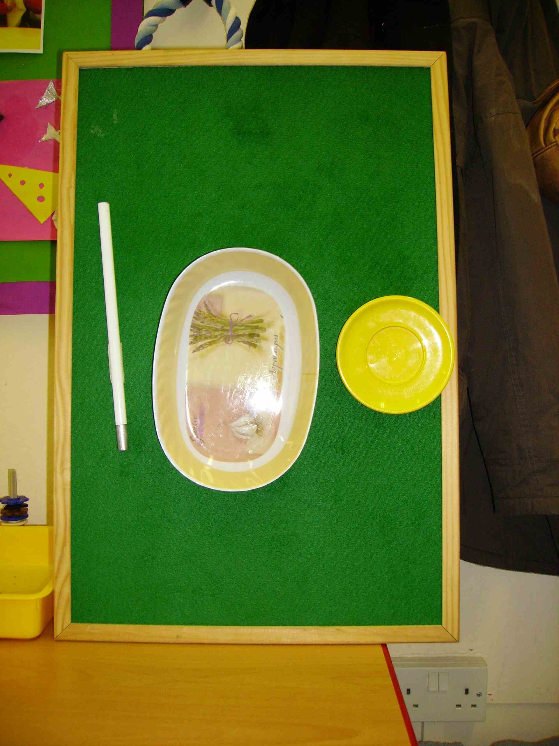 Sarah's timetable board. It displays the objects representing the first three activities taking place one school morning. From left to right they are part of a long cane, a dish and a small plastic plate.